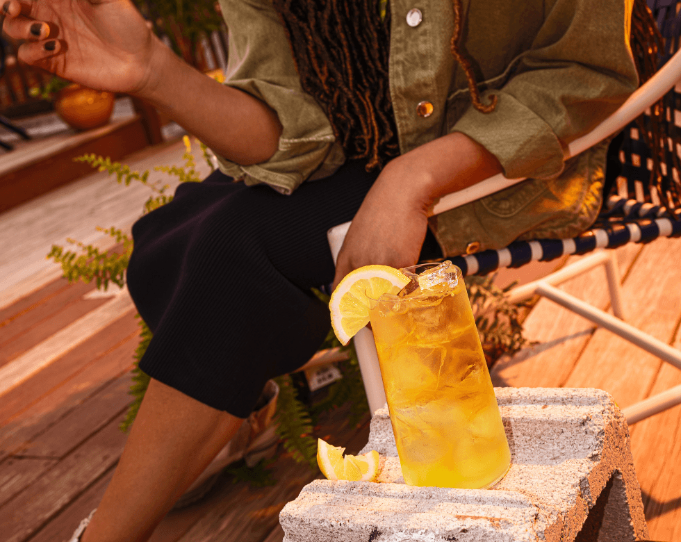 Picture of the jack apple fizz cocktail in a tall glass in front of a person sitting on a terrace lounge chair