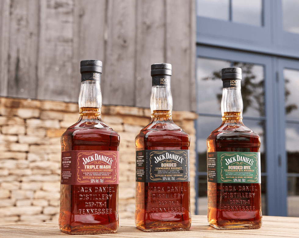 Picture of the three bottles of the Jack Daniel's Bonded Series in front of the Jack Daniel's Distillery