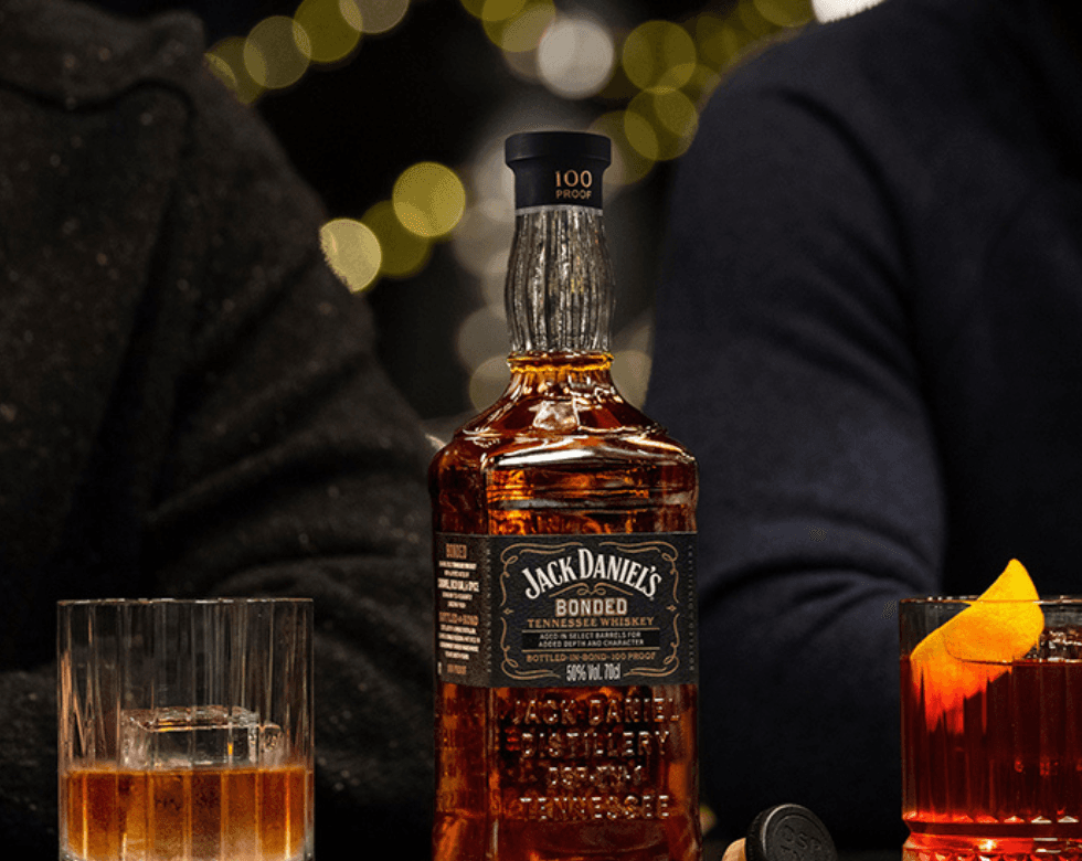 Picture of a Jack Daniel's Bonded bottle between two cocktail glasses and two people sitting behind it